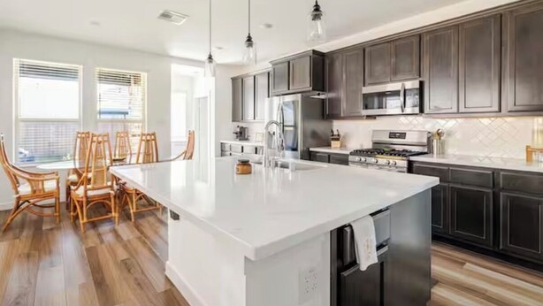 A modern kitchen with dark wood cabinets, a large island with a sink, and a dining area with wicker chairs. - Wonderful 4-bedroom house with AC in tranquil Houston neighborhood (Houston)