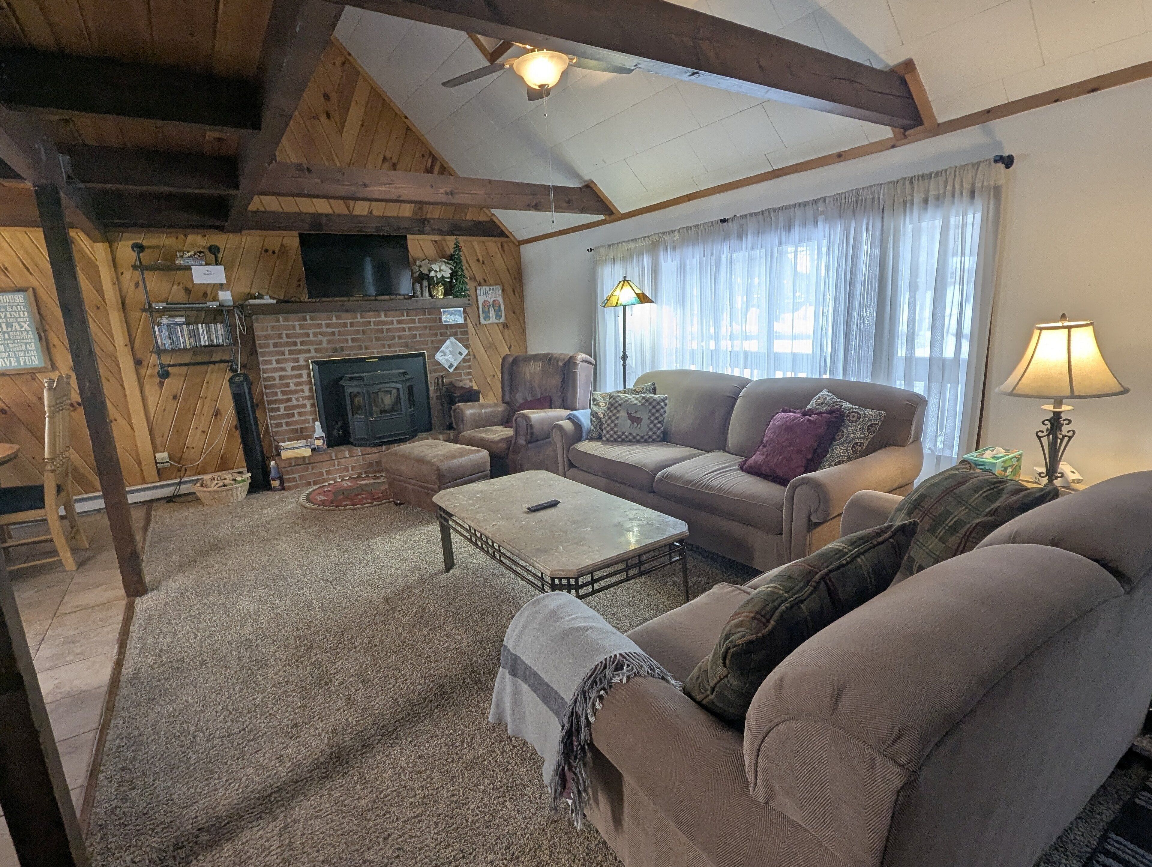 A cozy living room with a fireplace, comfortable seating, and a ceiling fan.