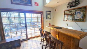 A room with a wooden bar, a door leading to an outdoor deck, and a framed exit sign. - Two Adjacent Lakefront Homes w/Docks, Boats, Firepit – Sleeps 24 (Pocono Lake)
