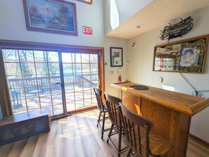 A room with a wooden bar, a door leading to an outdoor deck, and a framed exit sign. - Two Adjacent Lakefront Homes w/Docks, Boats, Firepit – Sleeps 24 (Pocono Lake)