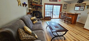 A living room with a stone fireplace, a wooden coffee table, a gray sofa with patterned cushions, and a bar area with wooden chairs. - Two Adjacent Lakefront Homes w/Docks, Boats, Firepit – Sleeps 24 (Pocono Lake)