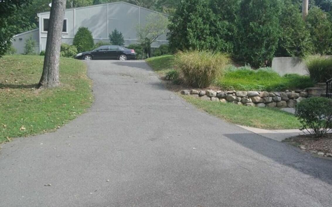 A residential driveway leading to a house with a stone wall and greenery.