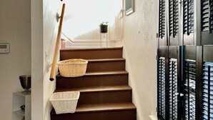 Una escalera con un tapiz decorativo, cestas y una ventana con persianas.