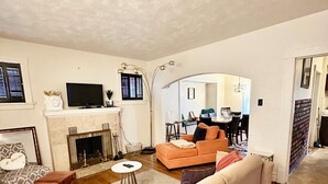 Una sala de estar con sofá, chimenea, televisor y un comedor visible a través de un arco.