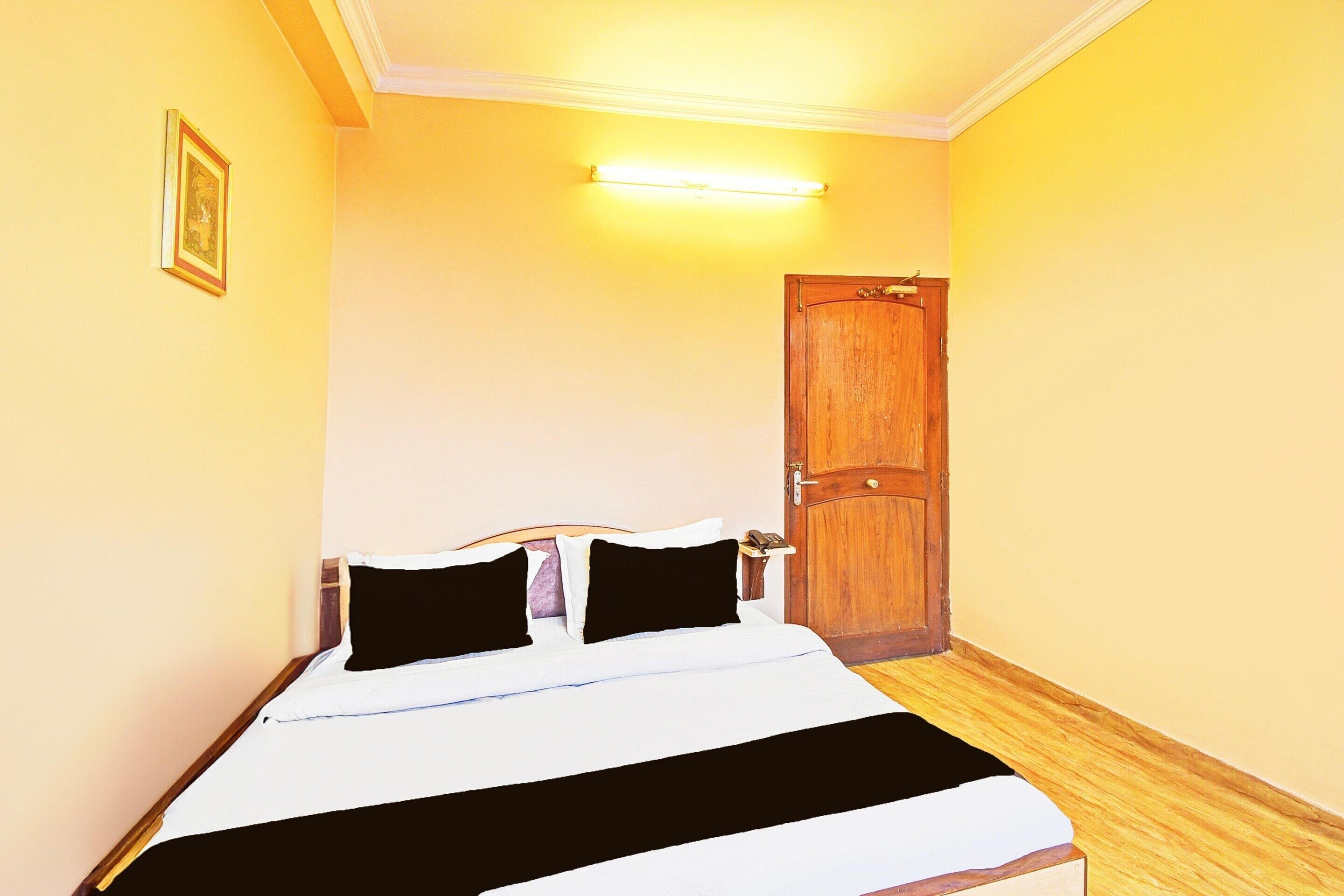 A hotel room with a bed, a wooden door, and a wall-mounted light fixture.