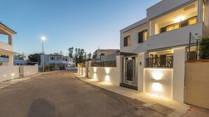Un carrer residencial amb cases modernes, una entrada tancada i il·luminació exterior.