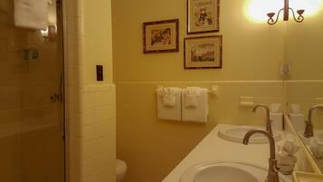 A bathroom with a shower, two sinks, a toilet, and framed pictures on the wall.