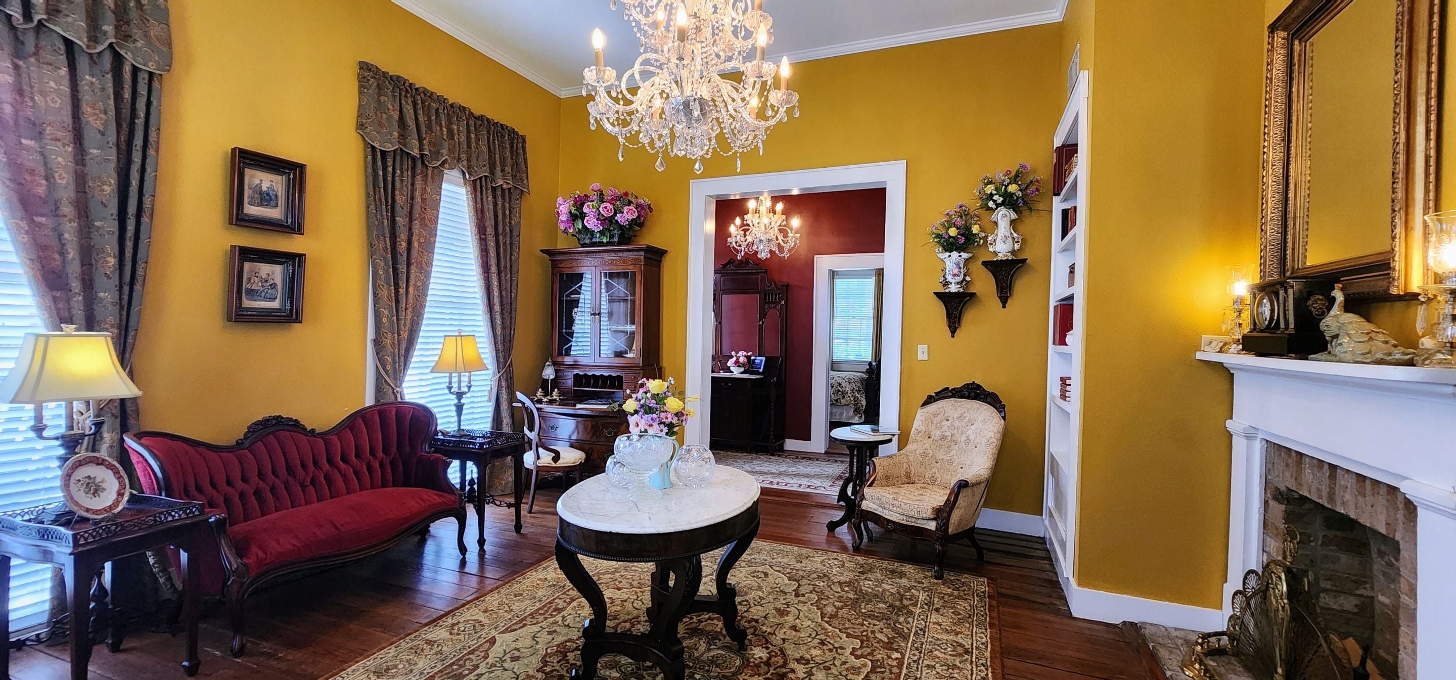 A room with a red sofa, a round table, a chandelier, and a fireplace.