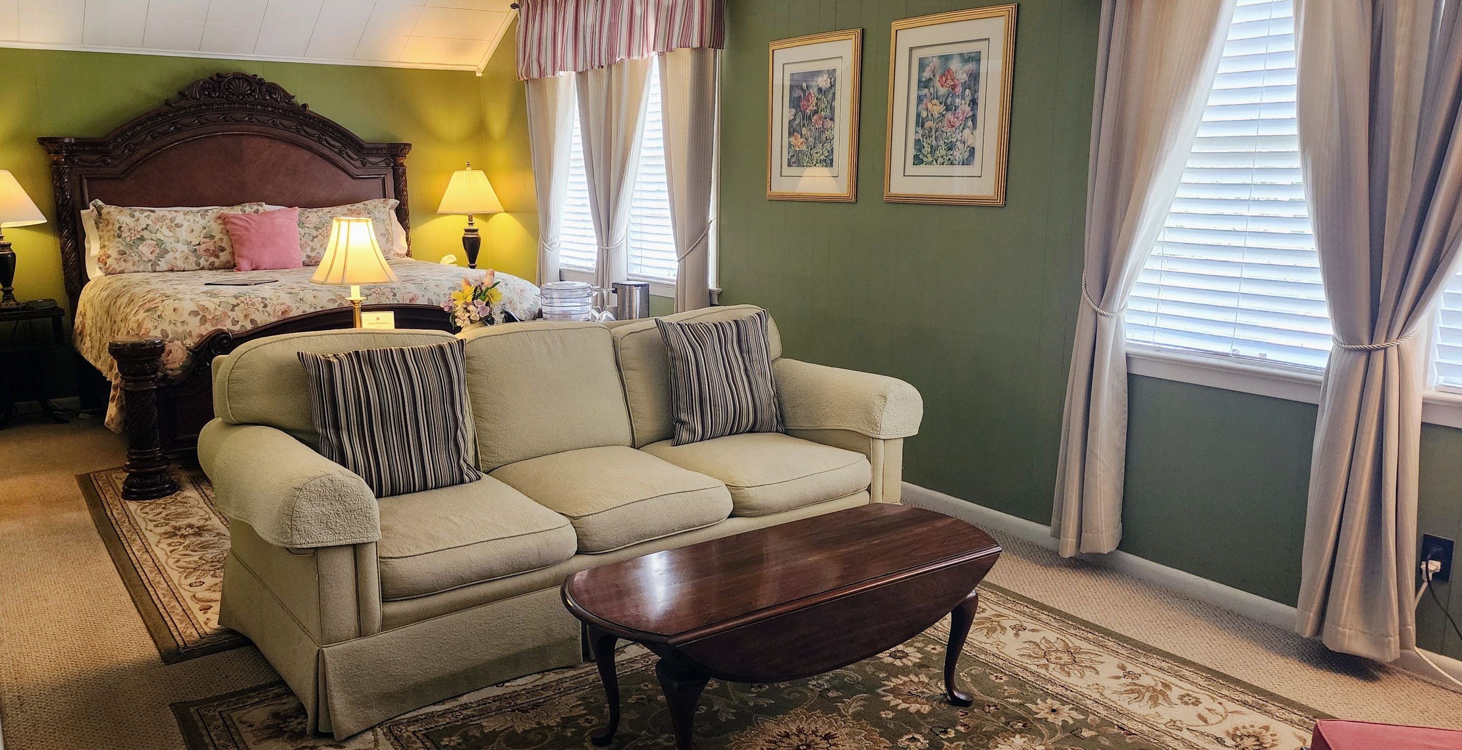 A room with a bed, a sofa, a coffee table, and two framed pictures on the wall.