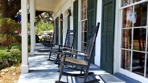 A porch with rocking chairs and a white building with green shutters. - Andrew Morris House Bed and Breakfast (Natchitoches)