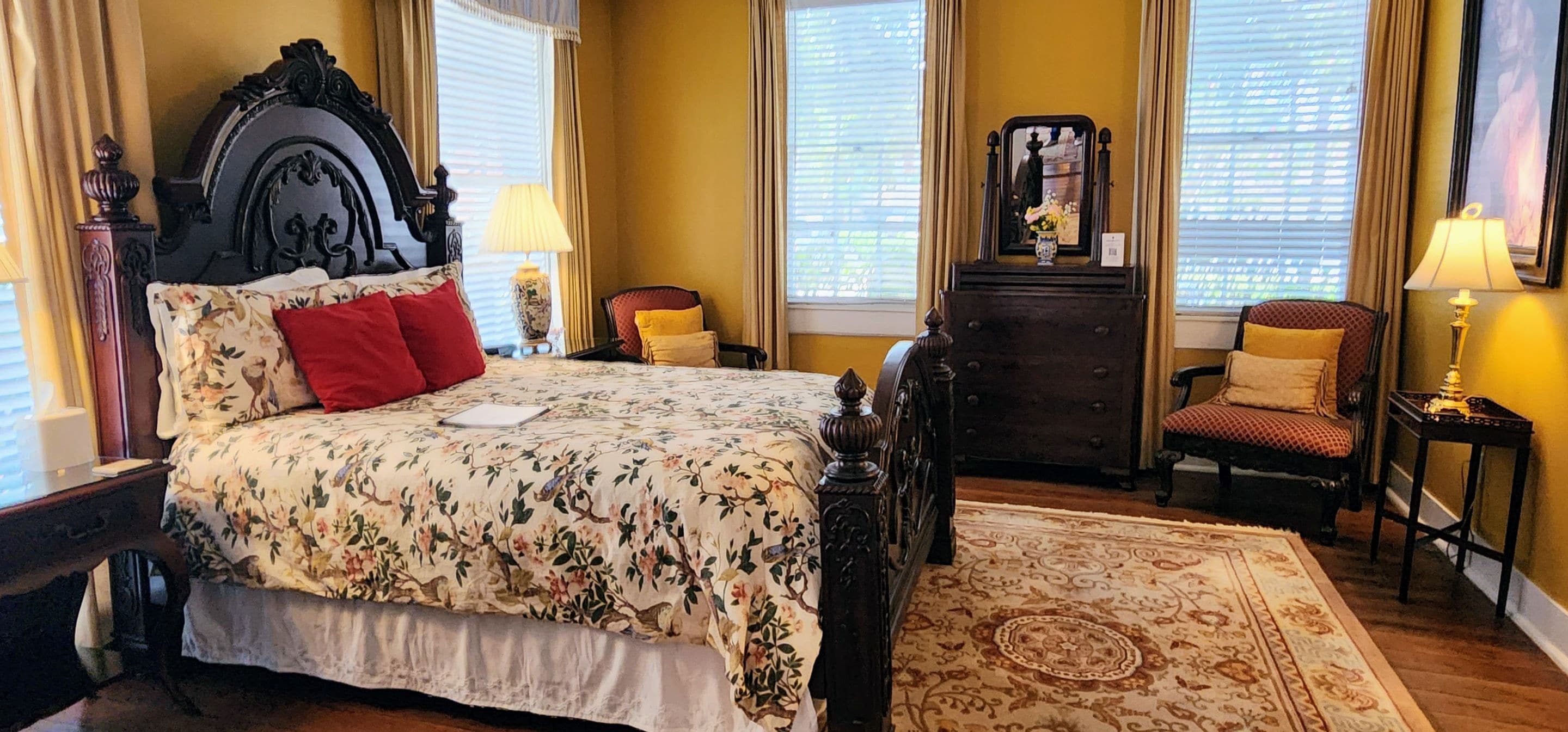A bedroom with a large bed, two chairs, a dresser, and a mirror.