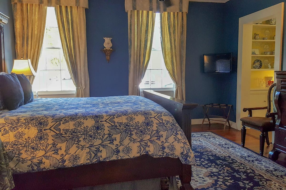 A bedroom with a bed, a dresser, a TV, and a window with curtains.