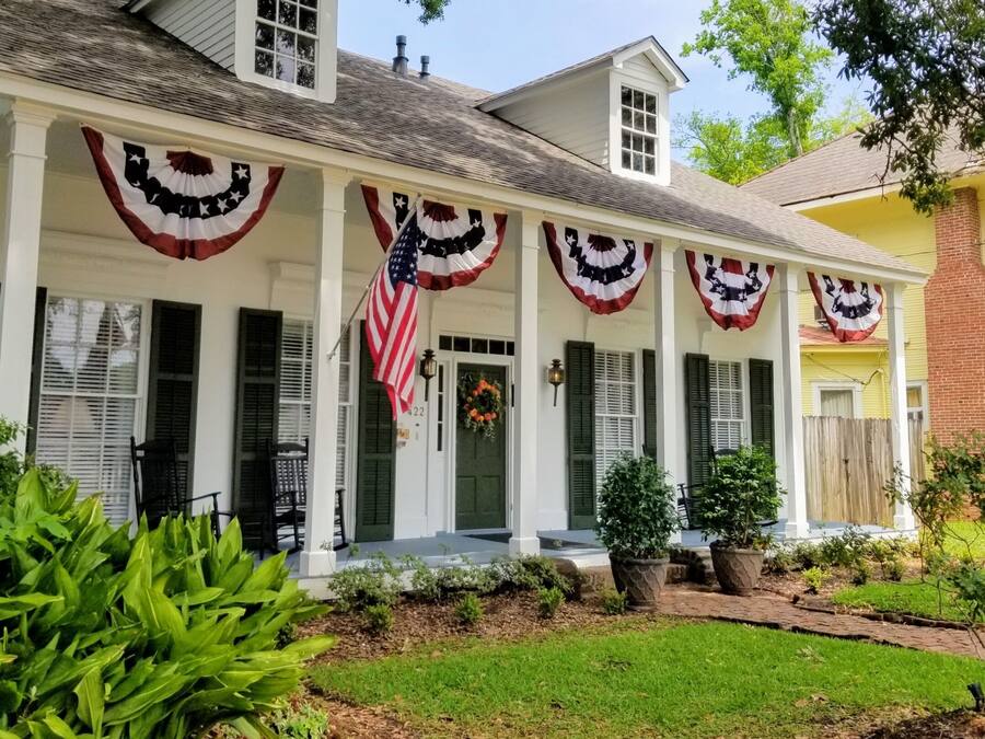 A historic house with a porch decorated with American flags and a sign indicating it is a bed and breakfast.