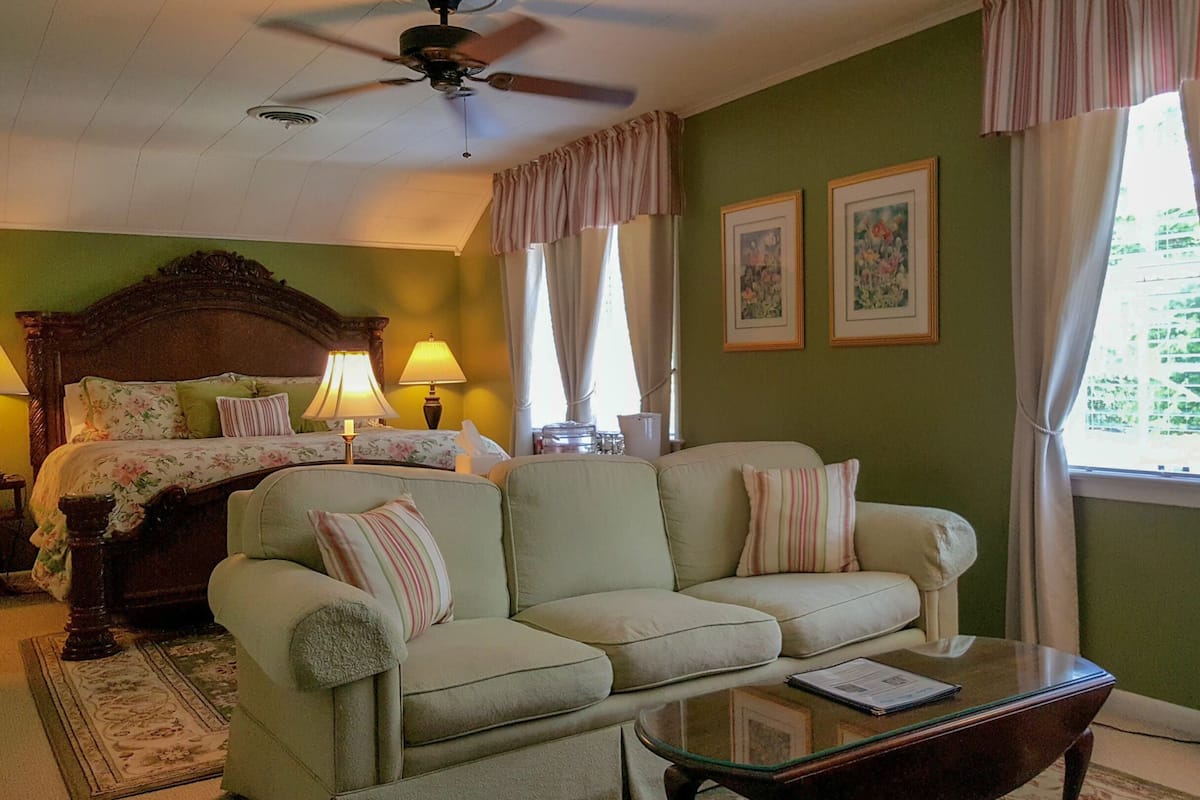A hotel room with a bed, a sofa, a coffee table, and two windows with curtains.