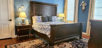 Un dormitorio con una cama de madera oscura, dos mesitas de noche con lámparas, una colcha con estampado floral y una alfombra estampada.