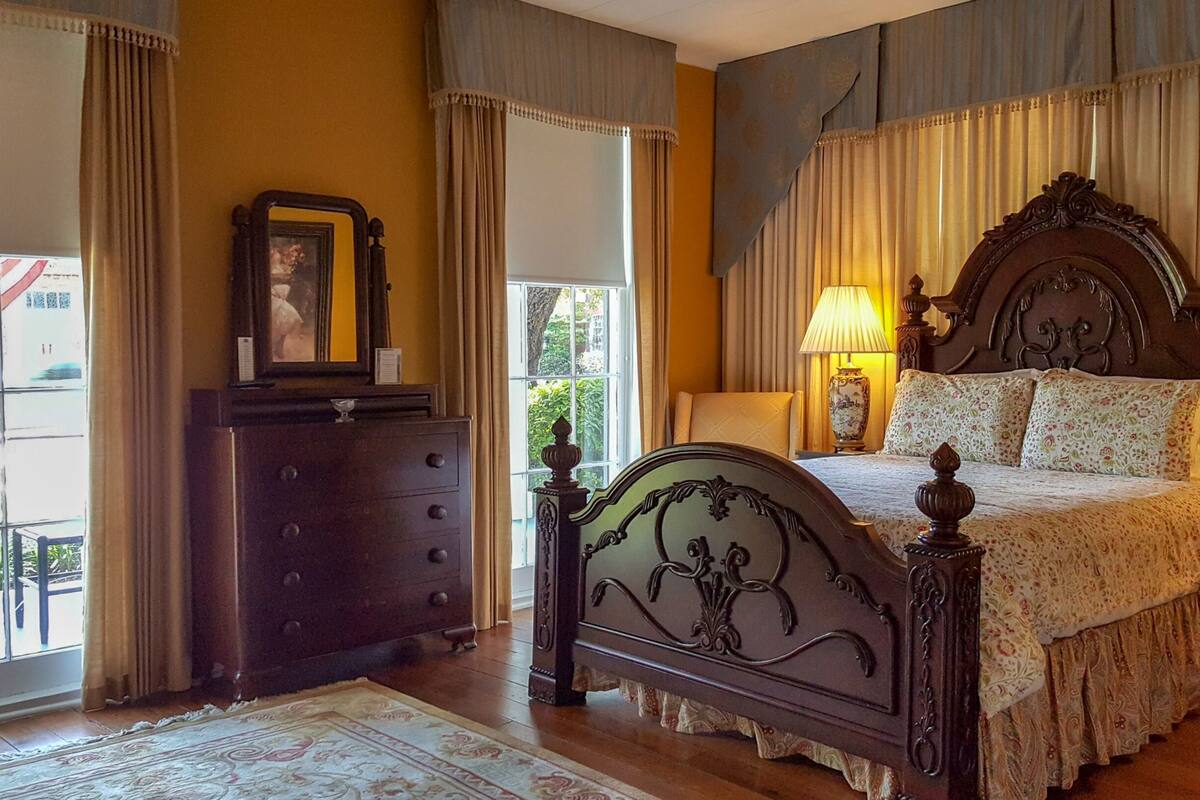 A bedroom with a wooden bed, two bedside lamps, a dresser, and a view of the outdoors.