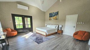 A bedroom with a bed, two chairs, a desk, a door, and a window.