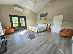 Ein Schlafzimmer mit Bett, zwei Stühlen, einem Schreibtisch, einer Tür und einem Fenster.