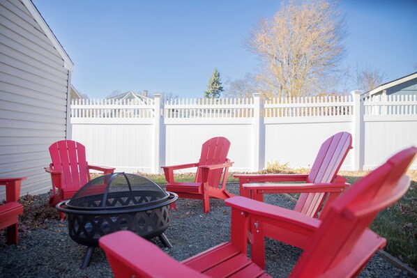 Un jardin avec une clôture blanche, des fauteuils Adirondack rouges et un foyer noir.