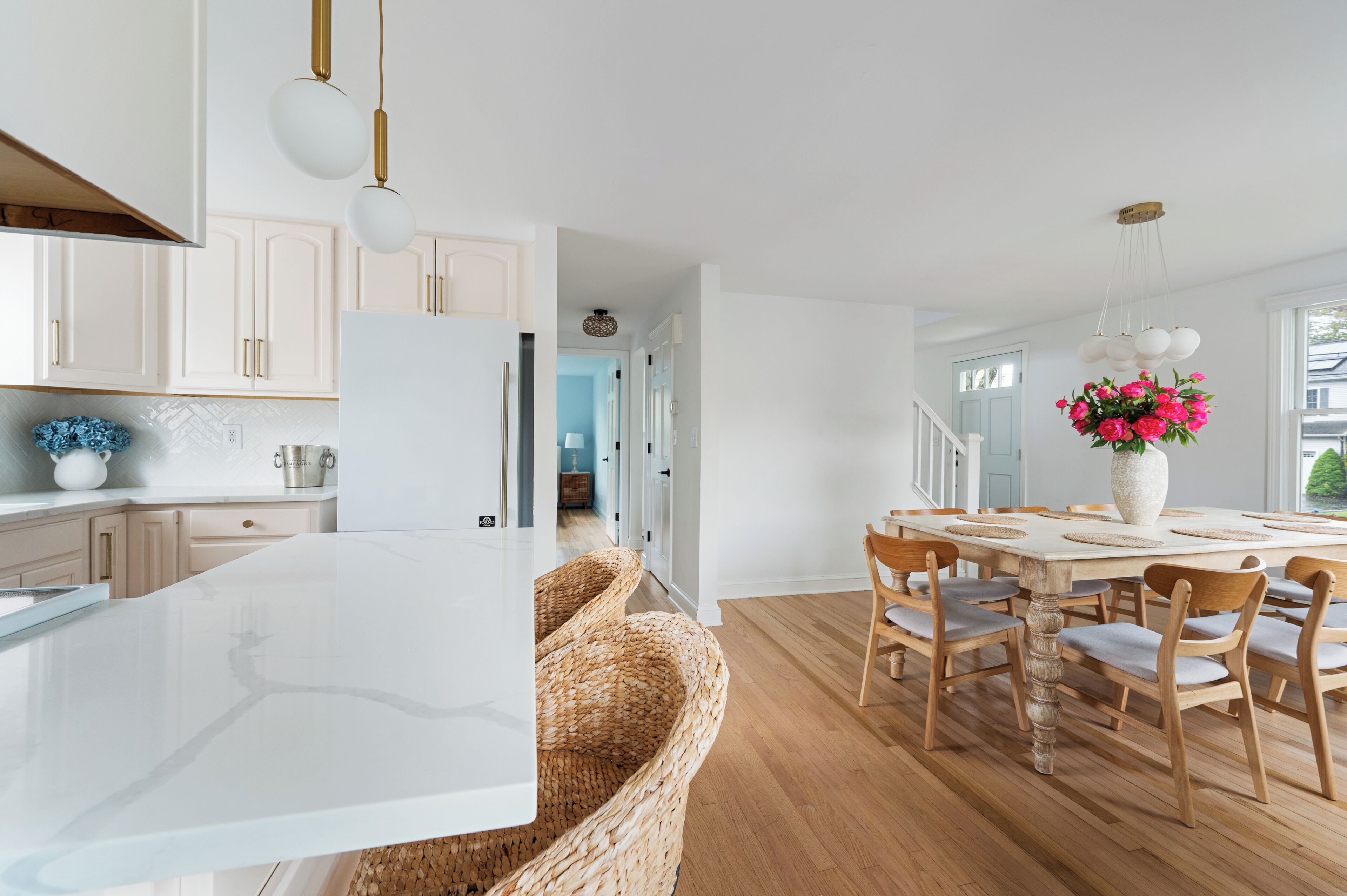 A modern kitchen with white cabinets, a large island, and a dining area with a wooden table and chairs.