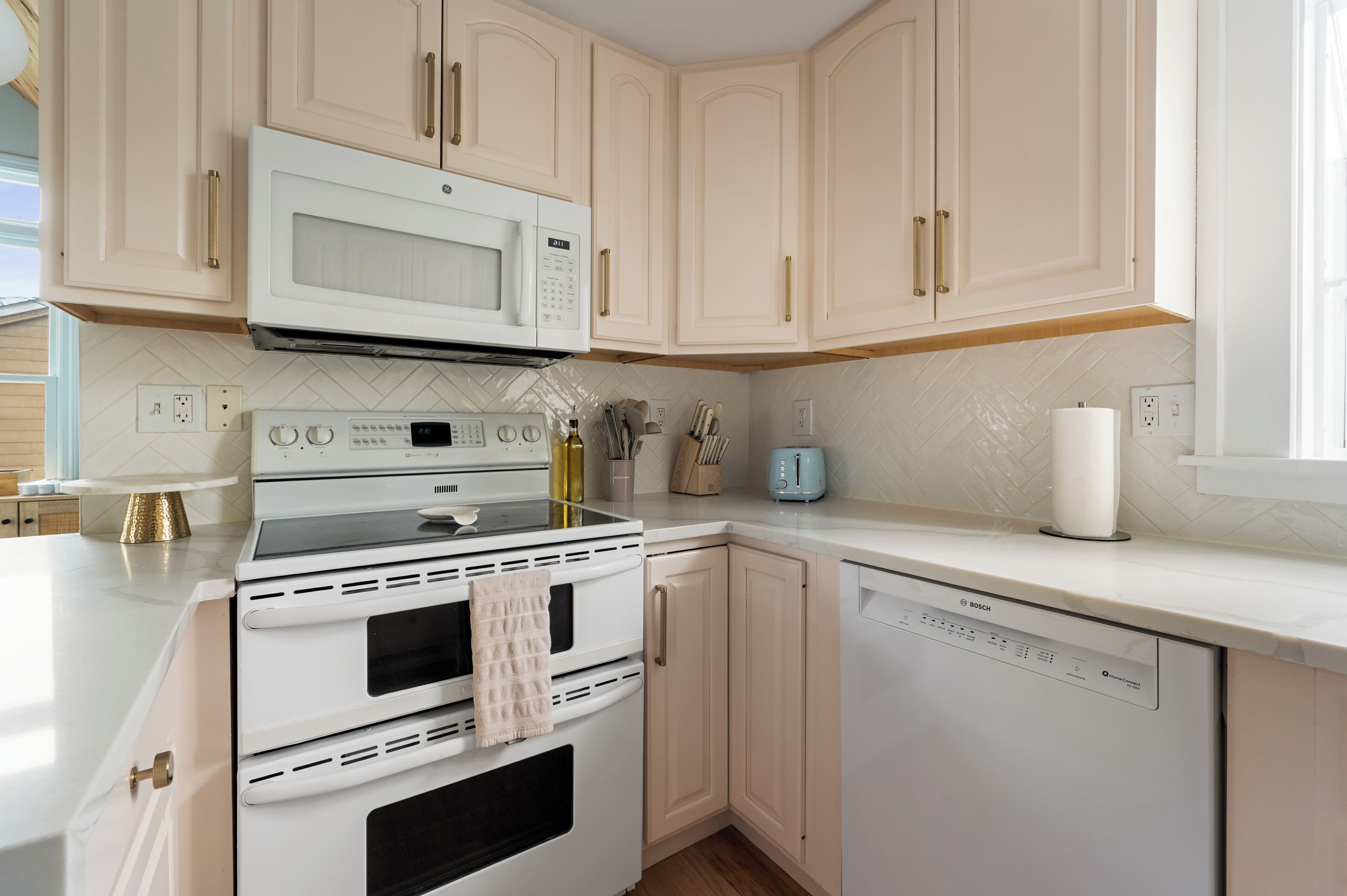 A kitchen with white appliances, beige cabinets, and a herringbone tile backsplash.