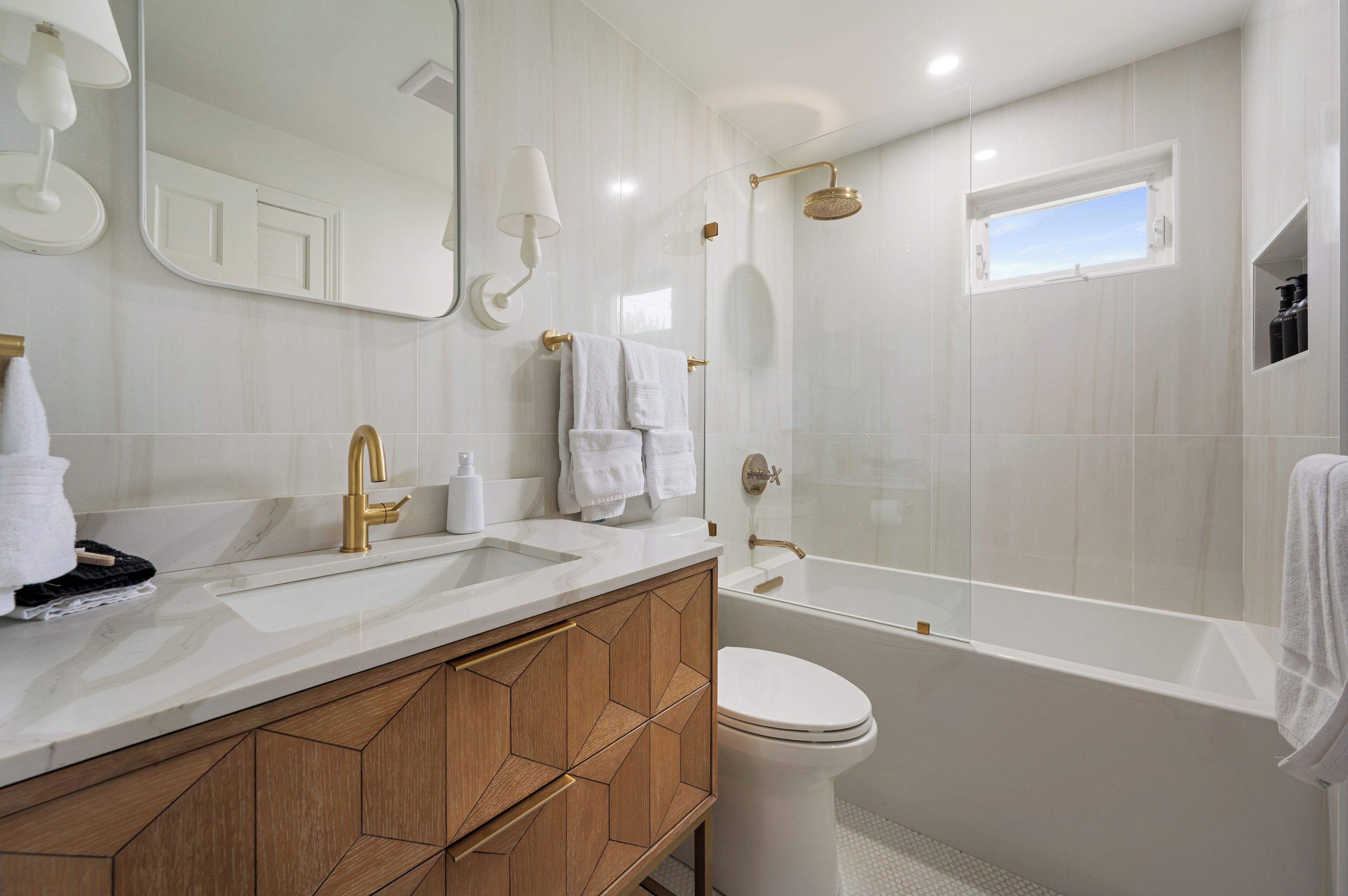 A modern bathroom with a large mirror, a bathtub, a toilet, and a shower area.