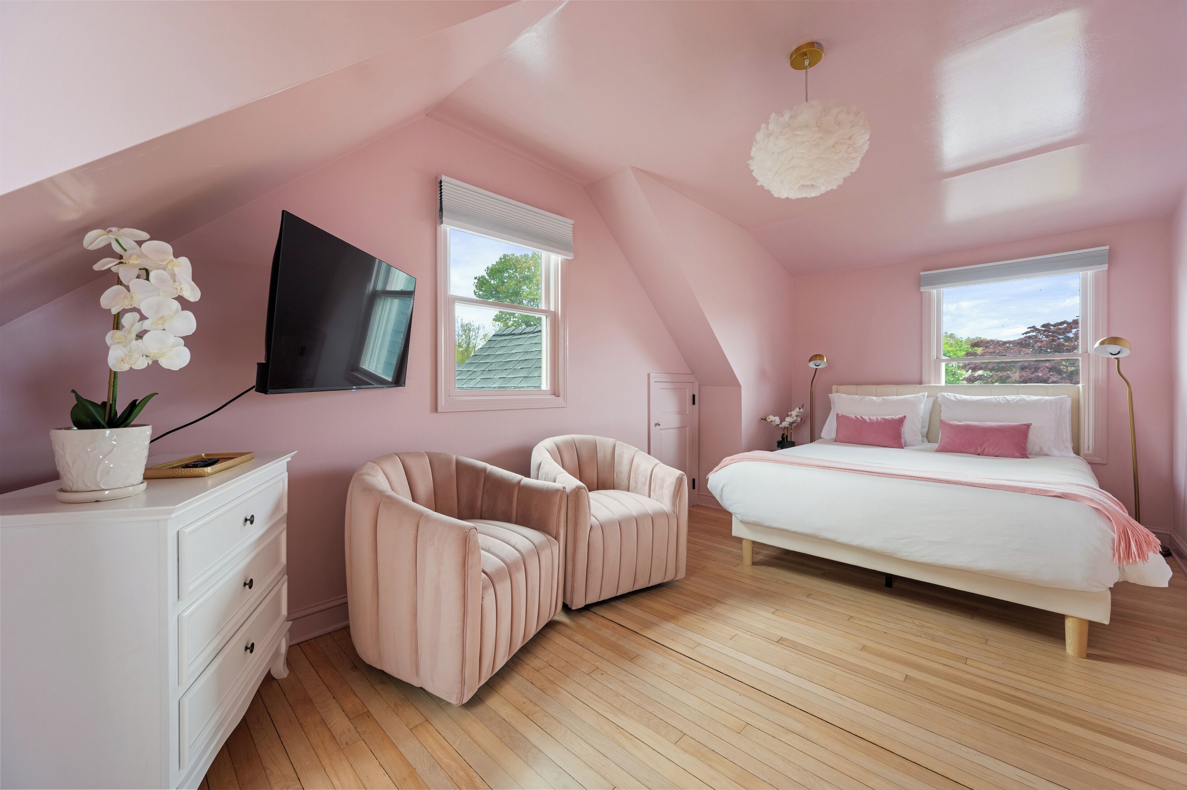Un dormitorio con una cama, dos sillas, un aparador, un televisor y dos ventanas.
