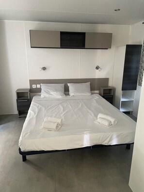A modern hotel room with a large bed, two bedside tables, a flat-screen TV mounted on the wall, and a small shelf unit. - 4* campsite, the lake of dreams near the Mediterranean and the Petite Camargue (Lattes)