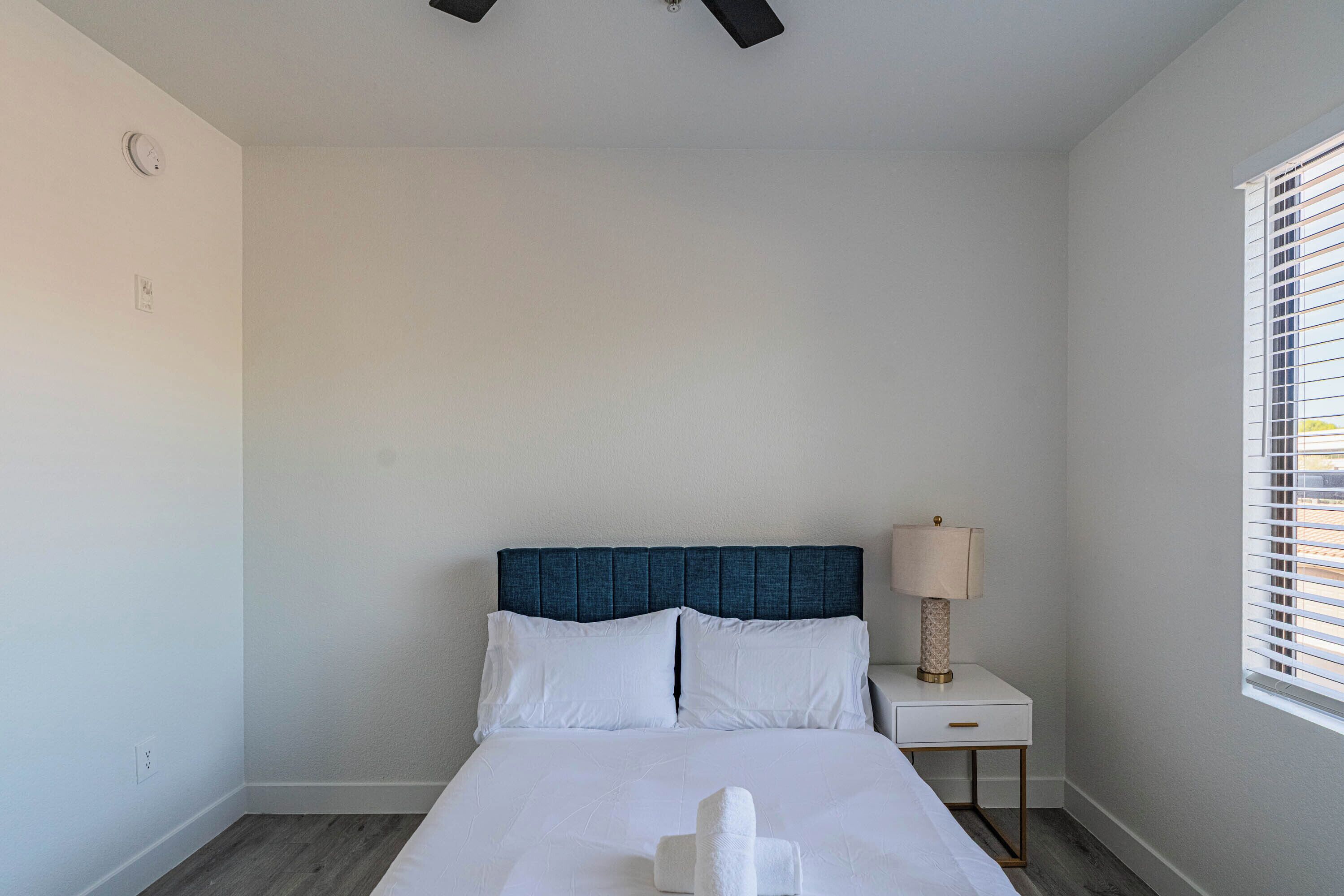 A neatly arranged hotel room with a bed, a bedside table with a lamp, and a window with blinds.