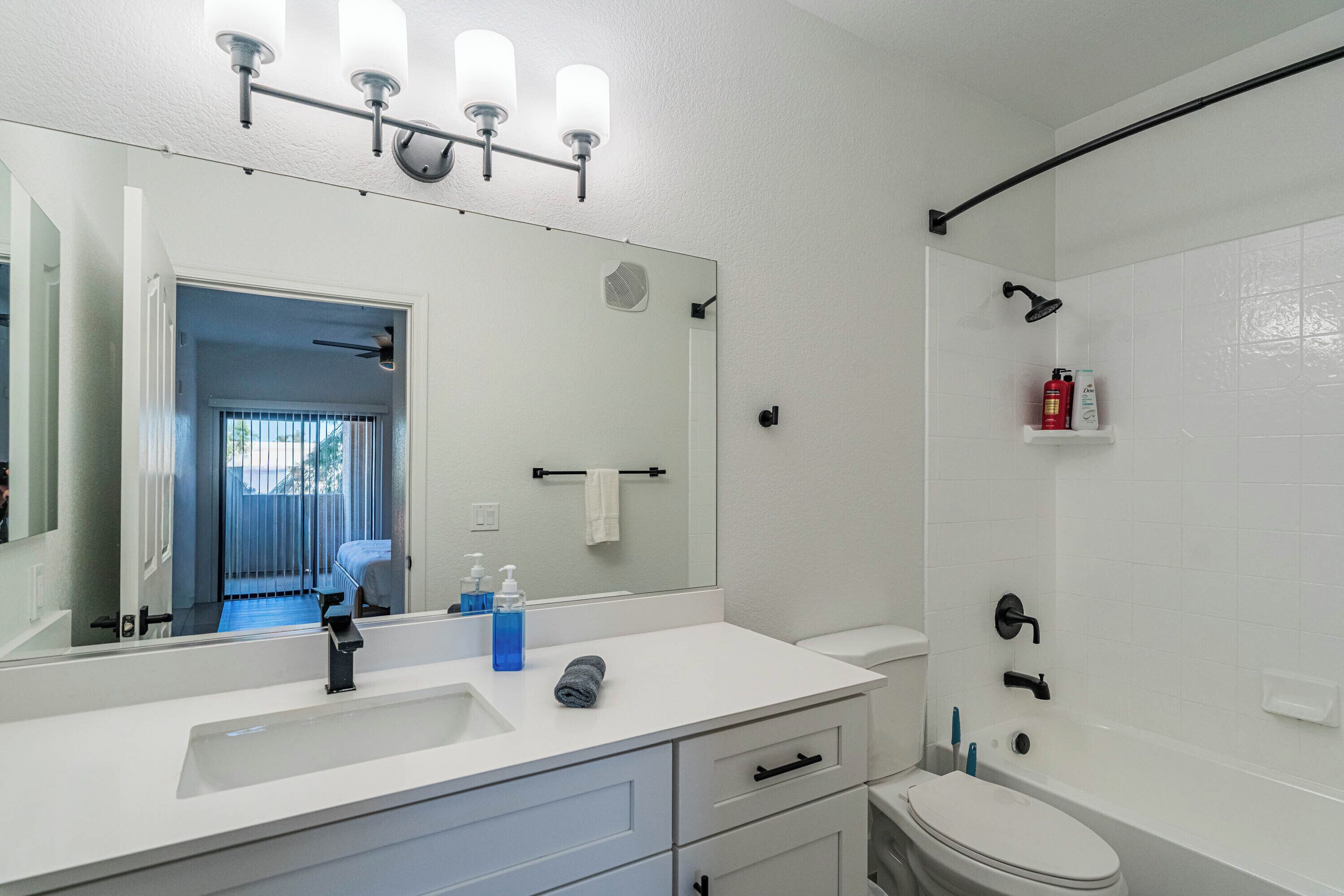 A modern bathroom with a white sink, mirror, and toilet. There is a shower area with a black curtain and a towel rack.