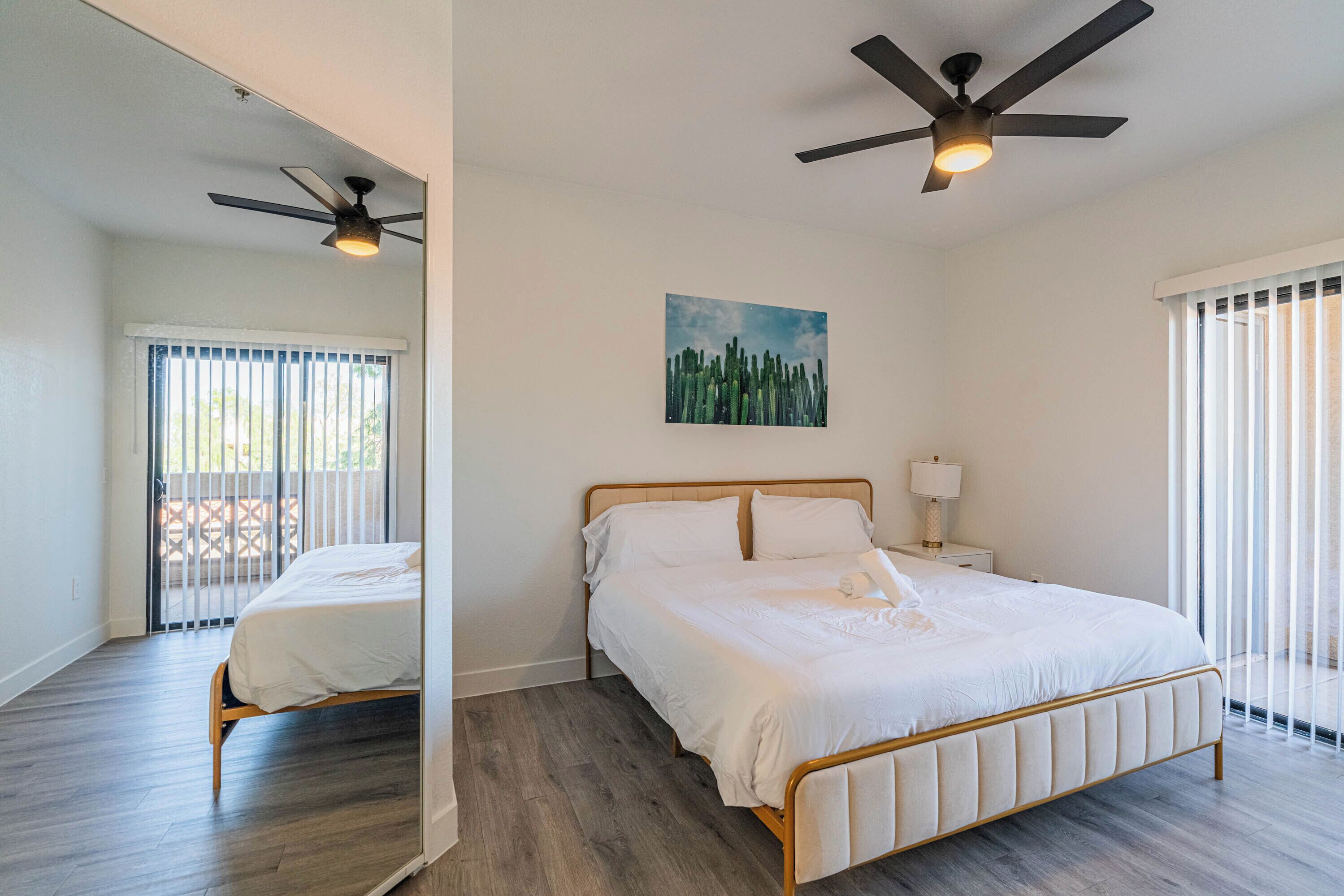 A bedroom with a bed, a ceiling fan, a nightstand with a lamp, and a window with blinds.