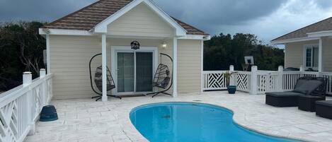 Un área de piscina techada con un deck blanco, dos sillas mecedoras y una puerta que da a un porche cubierto.