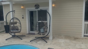En täckt uteplats med två gungstolar, en pool och en dörr som leder in till huset.