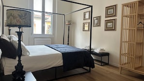 Un lit à baldaquin avec une tête de lit sombre, une table de chevet avec une lampe et une armoire en bois dotée d’une tringle pour suspendre les vêtements.