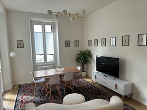 A modern living room with a dining area, a large TV, and a potted plant. - THE JASMINE FLORENCE (Firenze)