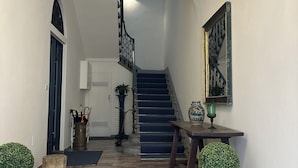 Une entrée imposante avec un sol en marbre, un escalier recouvert d’une moquette bleue et un lustre décoratif au plafond.