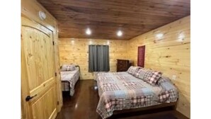 Quarto de cabana de madeira com duas camas, uma janela com cortinas e uma porta.