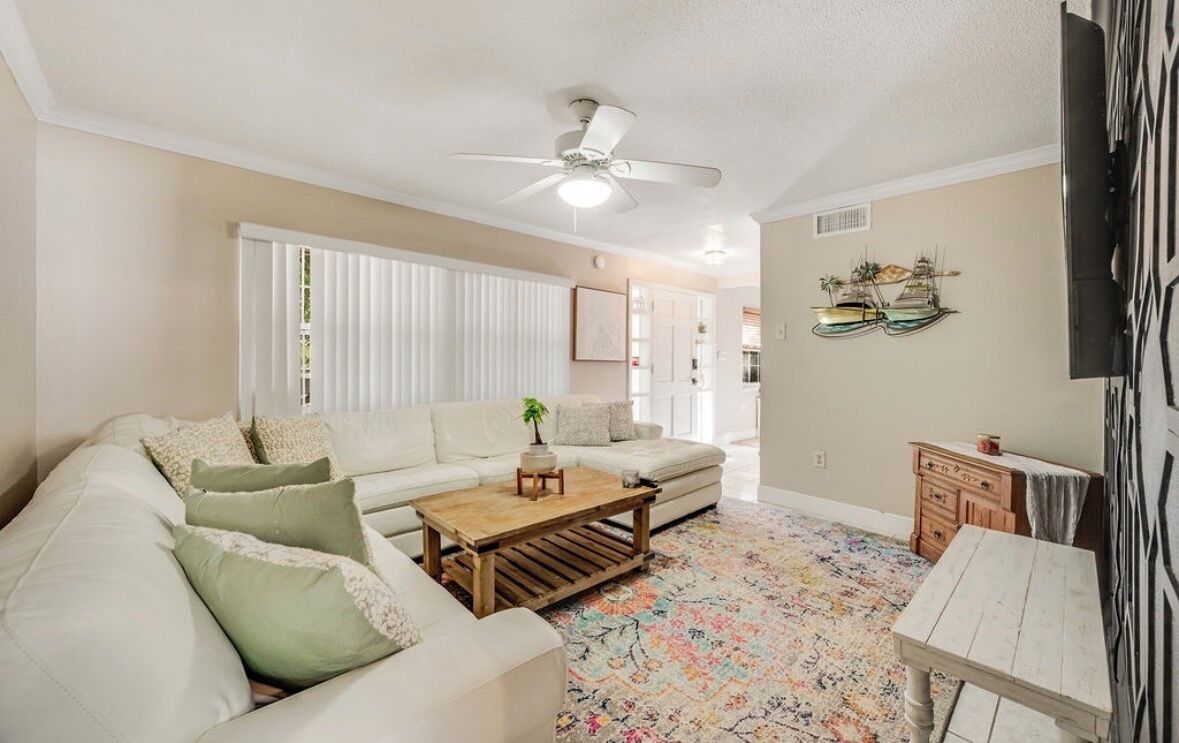 A living room with a white sofa, a wooden coffee table, a ceiling fan, and a colorful rug.