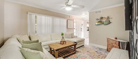A living room with a white sofa, a wooden coffee table, a ceiling fan, and a colorful rug.