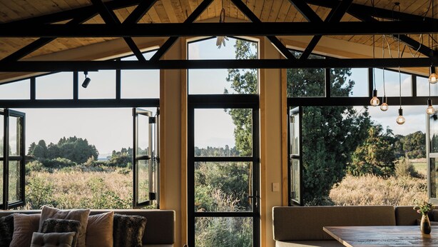 A room with large windows, a wooden ceiling, and a seating area with cushions.