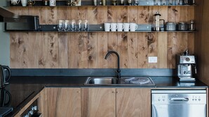 A modern kitchen with wooden cabinetry, a stainless steel dishwasher, and shelves with kitchenware.