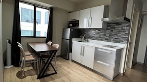 A compact kitchen with a dining table, chairs, a refrigerator, a stove, and a window with curtains. - STAYLUXIA Knightsbridge 1BR Suite w/ Balcony, FREE Pool Netflix, City View (Makati)