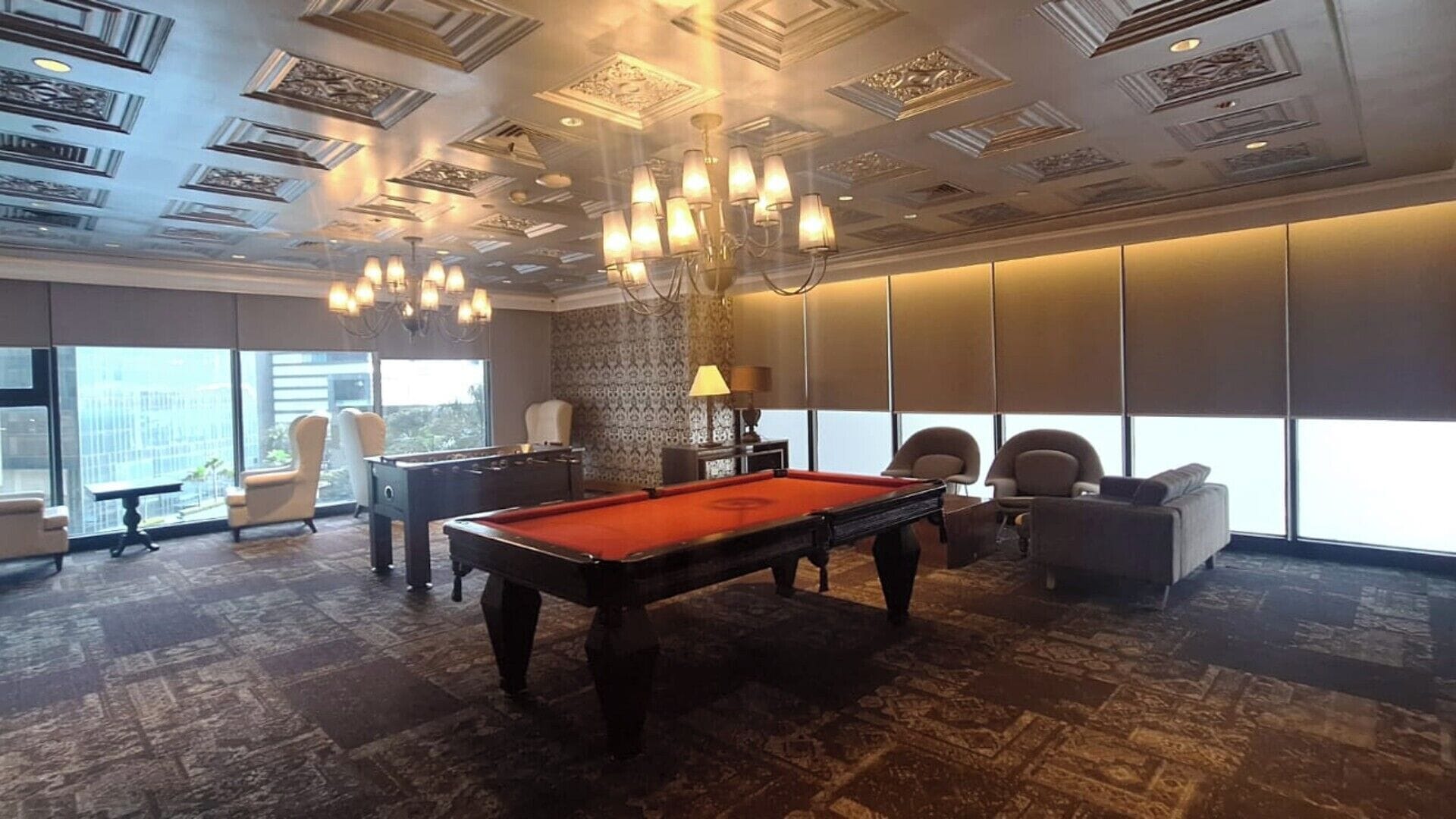 Una habitación con mesa de billar, sillas, un candelabro y ventanas amplias.