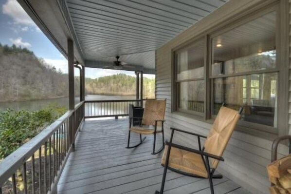 A covered porch with two rocking chairs, a view of a lake, and a forest in the background.