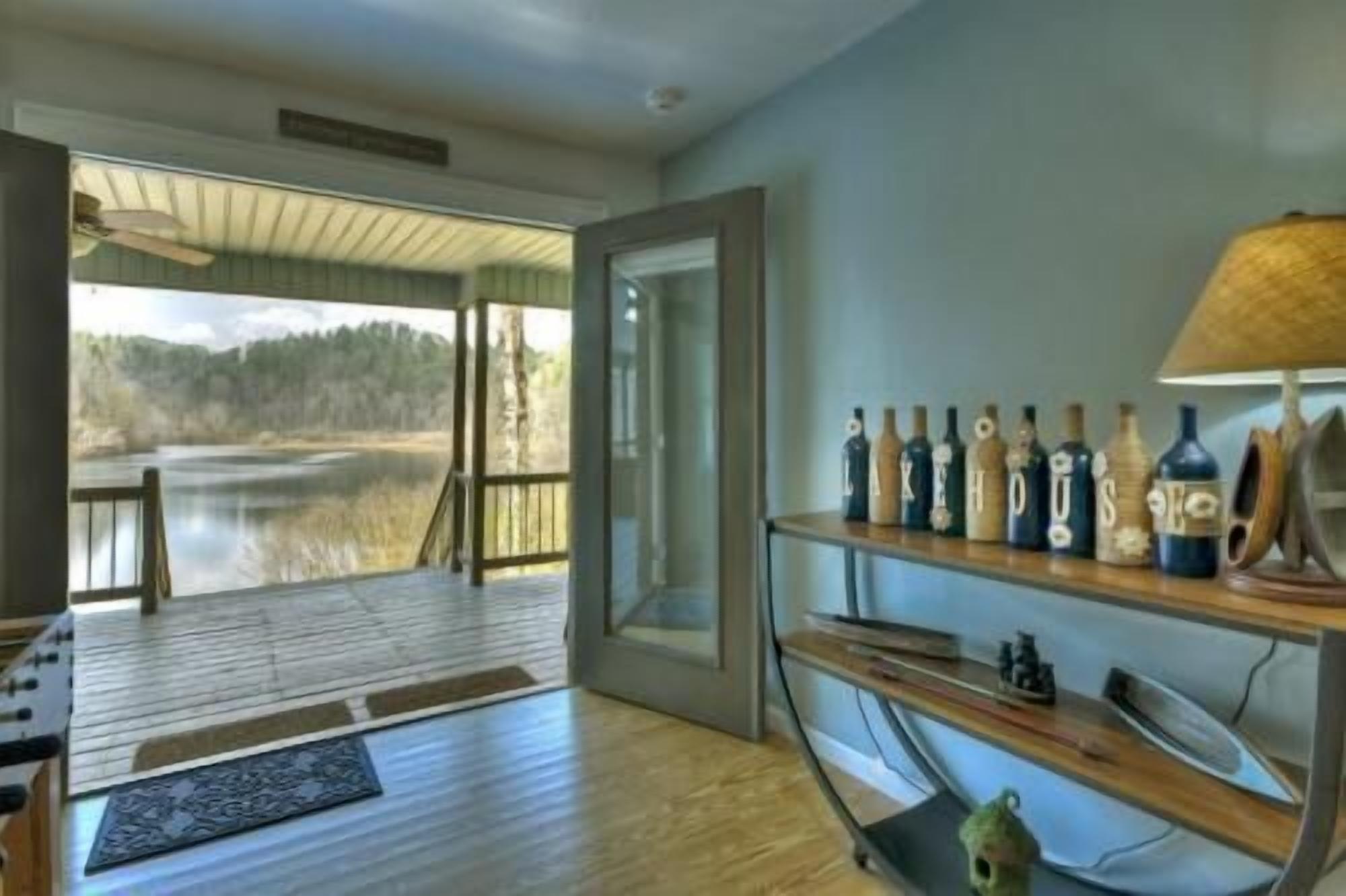 A room with a wooden floor, a glass door leading outside, and a shelf with bottles.