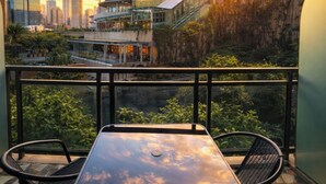 A balcony with a table and chairs, overlooking a cityscape with modern buildings and a sunset. - STAYLUXIA Gramercy 2BR Junior Suite w/Balcony Free Pool Gym Netflix & Amenities  (Makati)