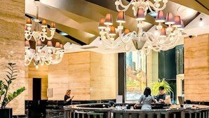 A modern lobby with a central reception desk, multiple chandeliers, and a large window offering a view of the cityscape. - STAYLUXIA Gramercy 2BR Junior Suite w/Balcony Free Pool Gym Netflix & Amenities  (Makati)
