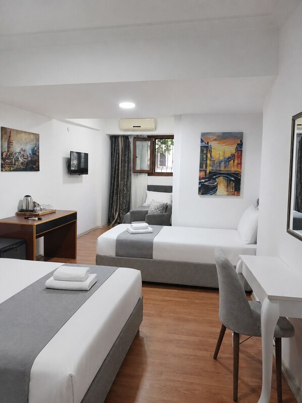 Habitación de hotel con dos camas, un escritorio, una silla, un televisor y pinturas en las paredes.