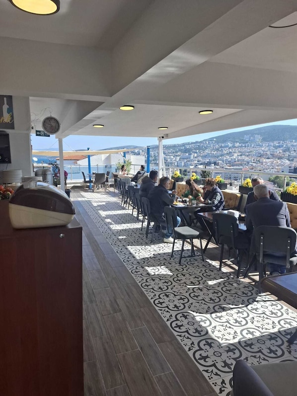 Un espacio exterior para comer con mesas y sillas, un reloj y vistas de la ciudad.