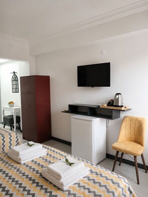 A hotel room with a bed, a desk, a wardrobe, a TV, a mini-fridge, and a chair.